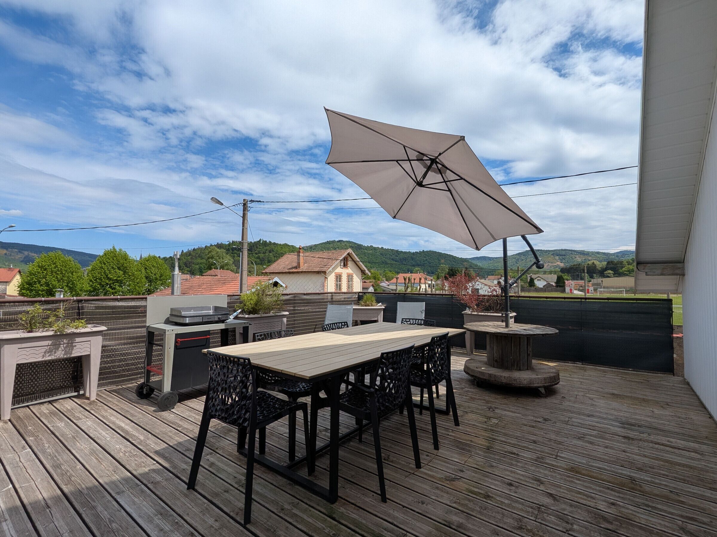 En udendørs terrasse med bord, stole, grill og stor parasol.