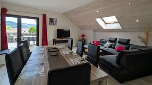 A modern living room with a dining area, a TV, and a balcony with red curtains.