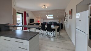 A modern kitchen with a dining area, featuring a large island, a built-in oven, and a refrigerator.