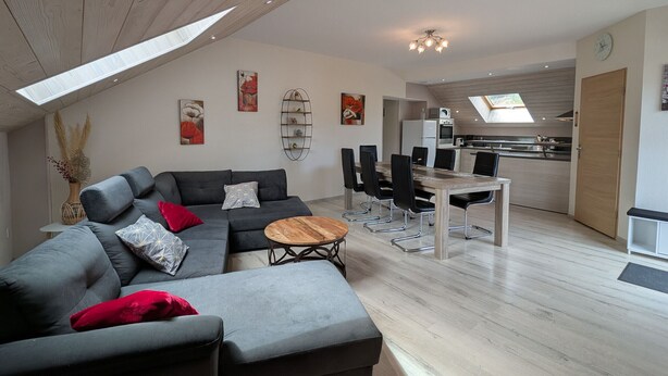A modern living room with a grey sectional sofa, a wooden coffee table, and a dining area with a white table and black chairs.