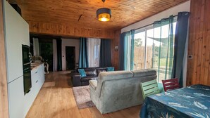 Un intérieur de chalet chaleureux avec un plafond en bois, un coin repas avec une table, un canapé et un coin cuisine équipé d’un réfrigérateur et d’une cuisinière.