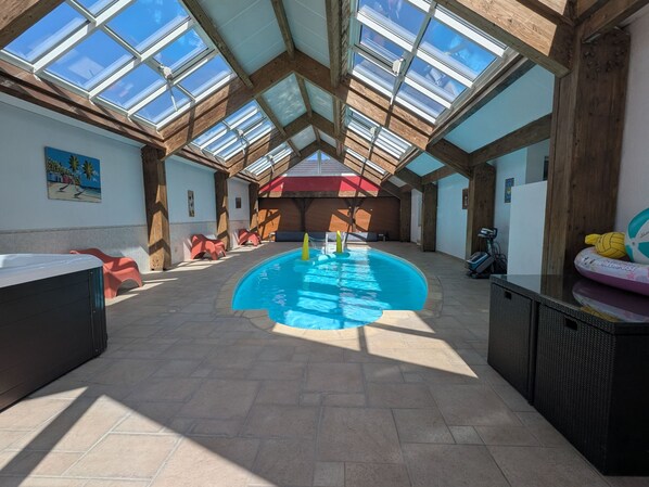 Una piscina interior con techos altos y tragaluces, rodeada de asientos y una mesa de billar.