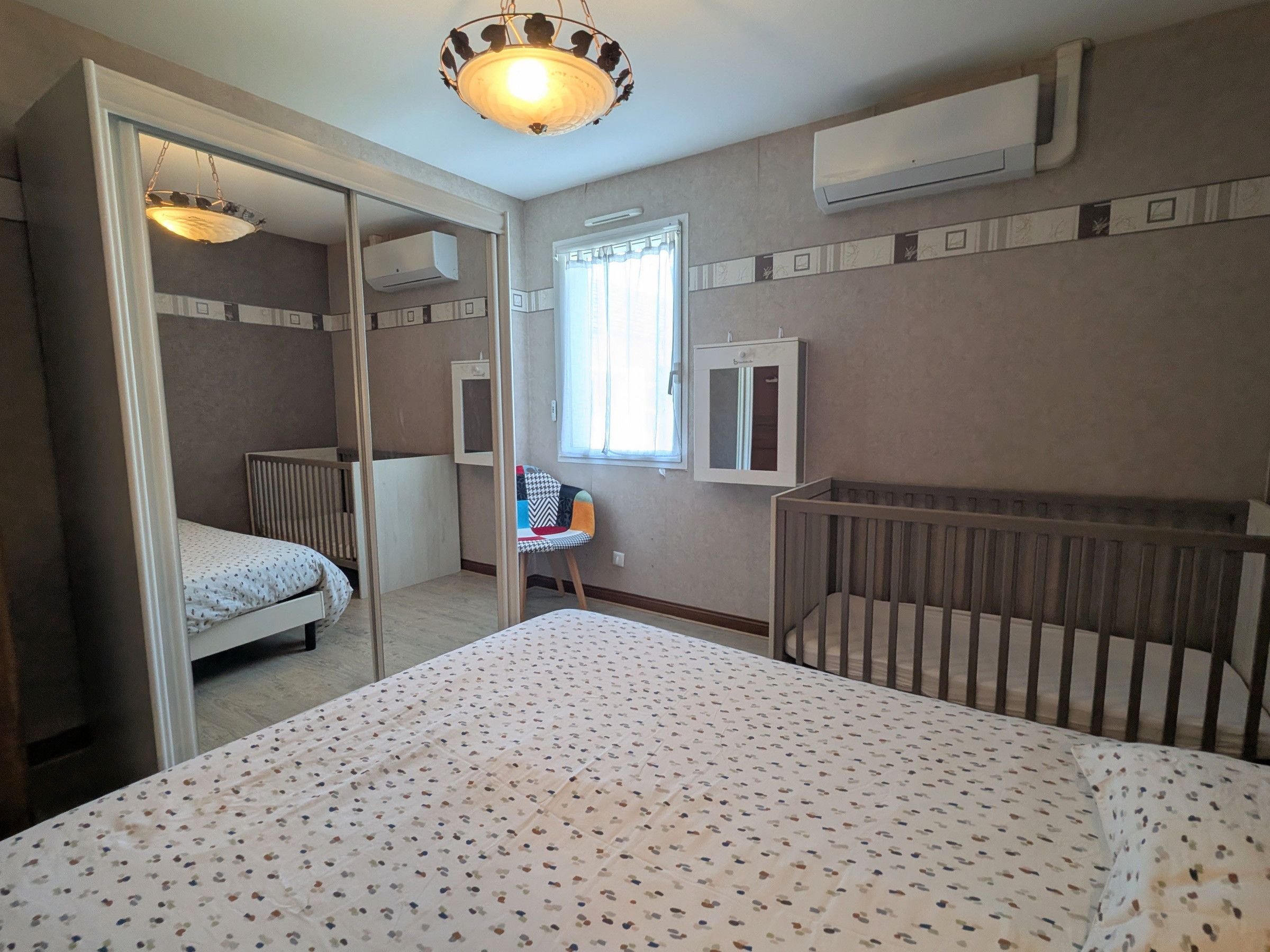 A bedroom with a bed, a crib, a chair, and a window.