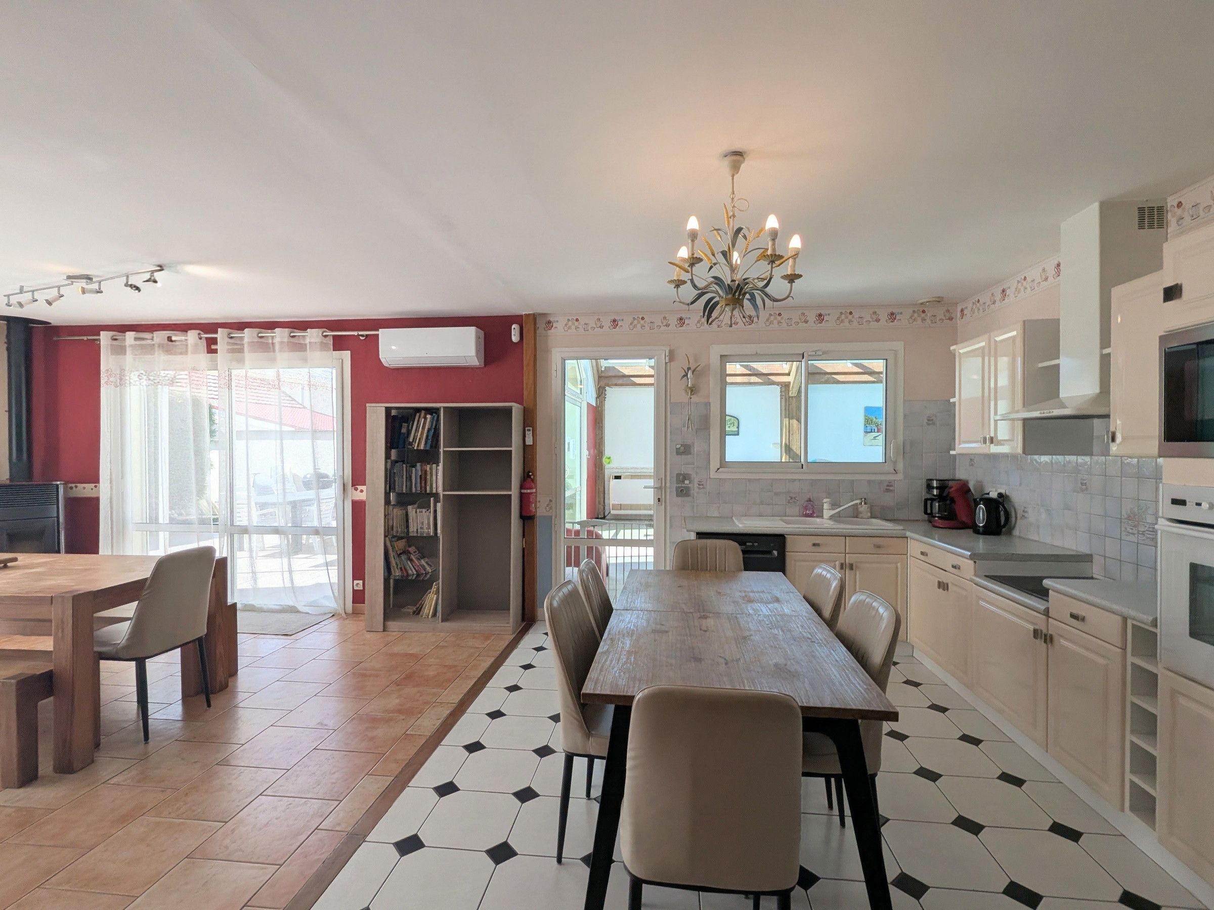 Une cuisine avec une table à manger, des chaises, un lustre et une vue sur l’extérieur.