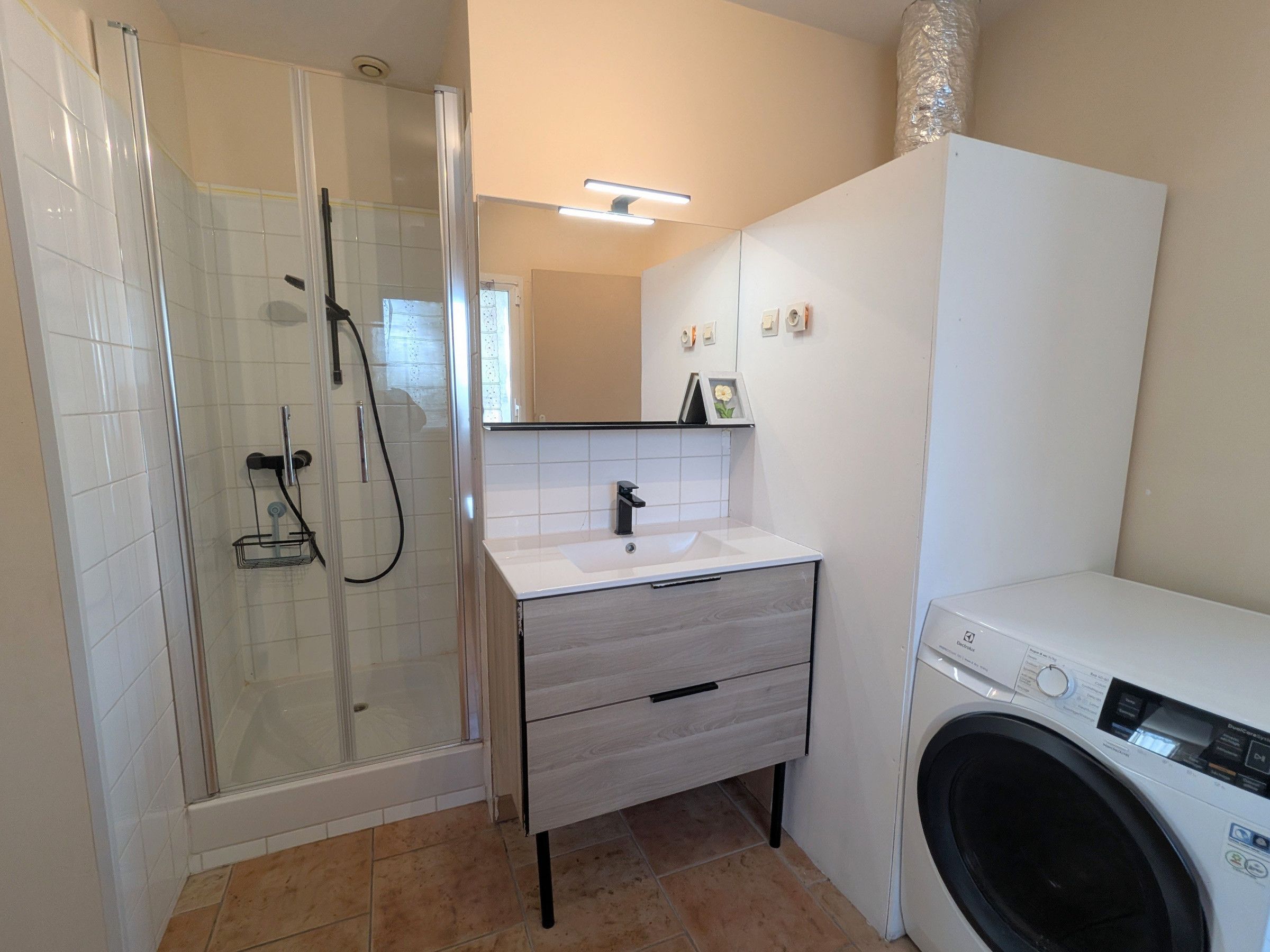Un baño moderno con ducha de vidrio, un lavamanos con espejo y una lavadora.