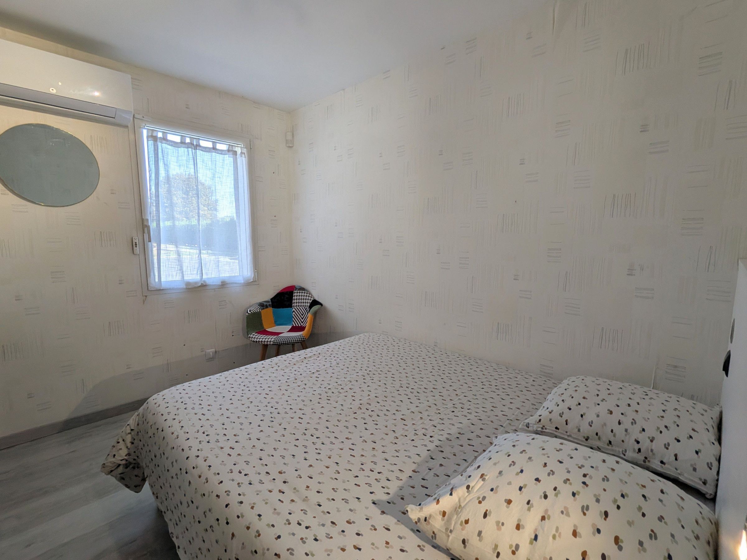 Ein Schlafzimmer mit Bett, Stuhl, Fenster und einer Wand-Klimaanlage.