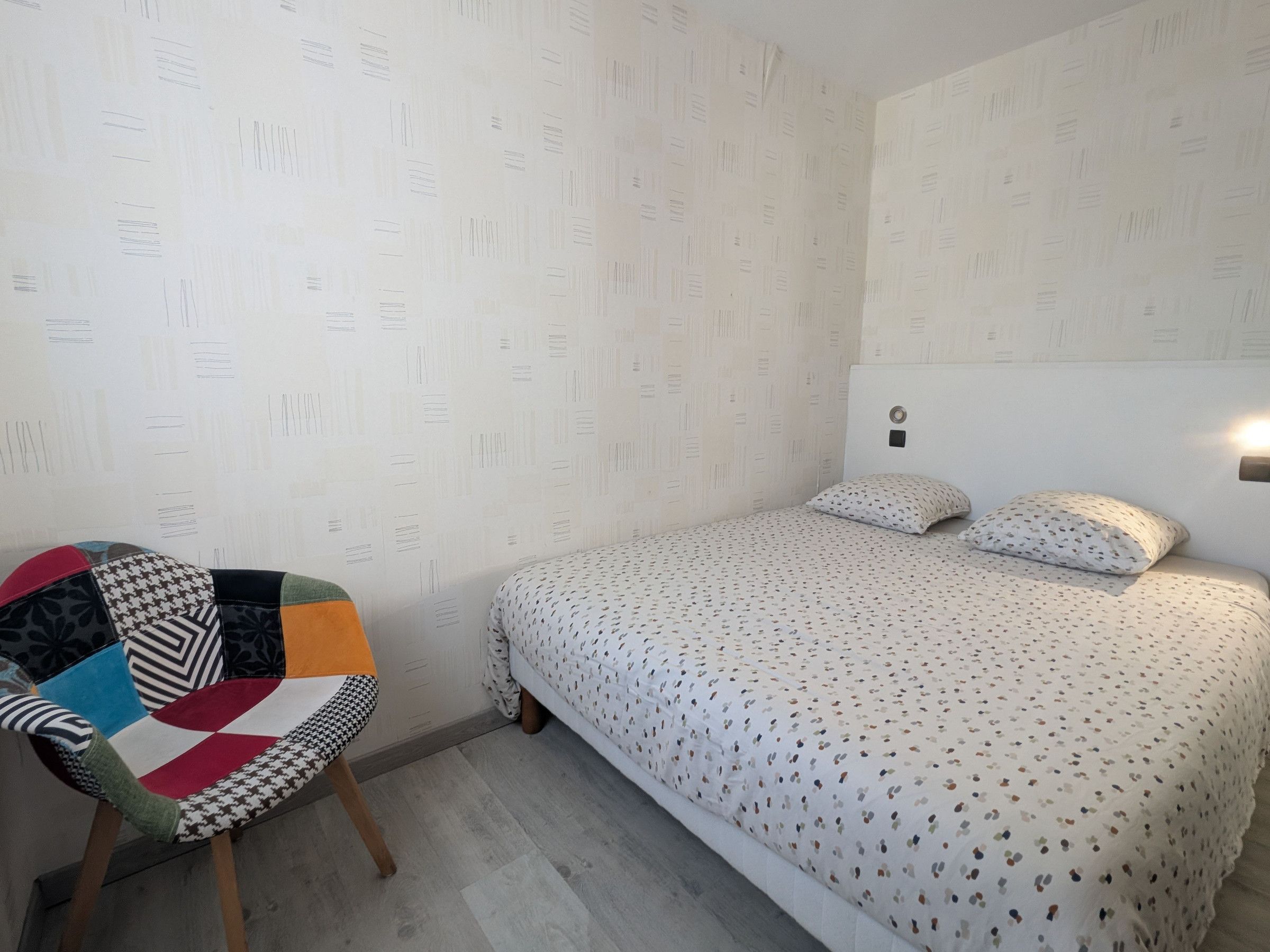 Quarto com cama, uma cadeira e parede com padrão.