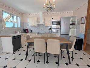 Una cocina con una mesa de comedor, sillas, lavavajillas, refrigerador y estufa.