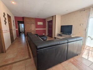 Un salon avec un canapé, un téléviseur et un couloir menant aux autres pièces.