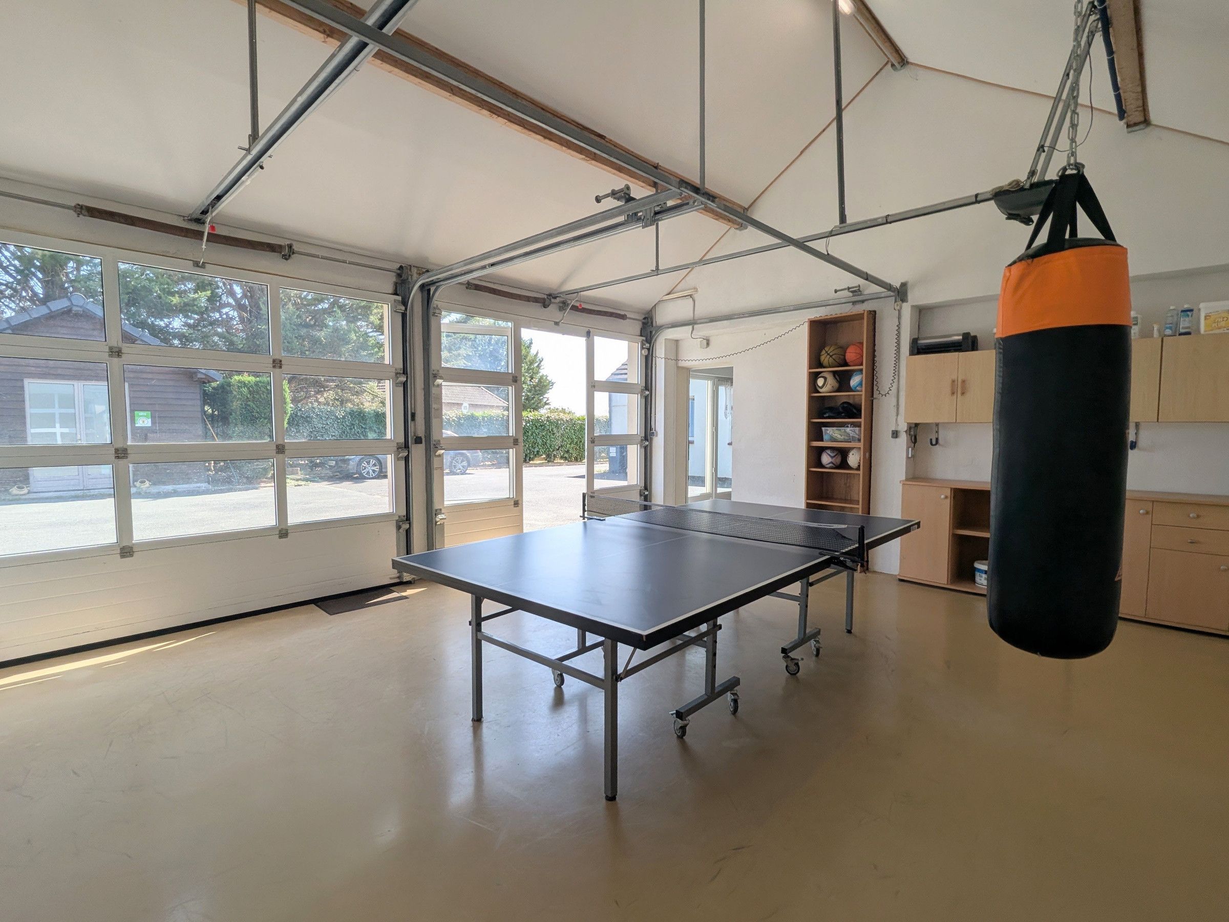 A spacious room with a ping pong table, a punching bag, and a basketball shelf.