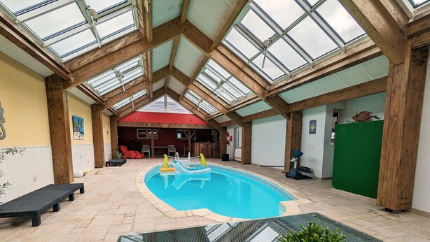 Une piscine intérieure dotée d’un toit en verre, de poutres en bois et d’un mur végétal.