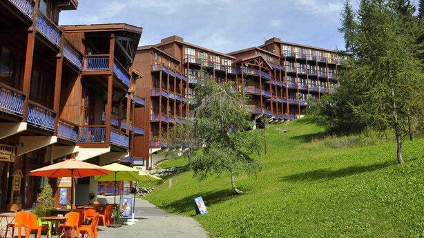 A hotel with multiple balconies, outdoor seating, and a grassy slope. - Calm duplex near slopes with balcony (Les Arcs 1800)