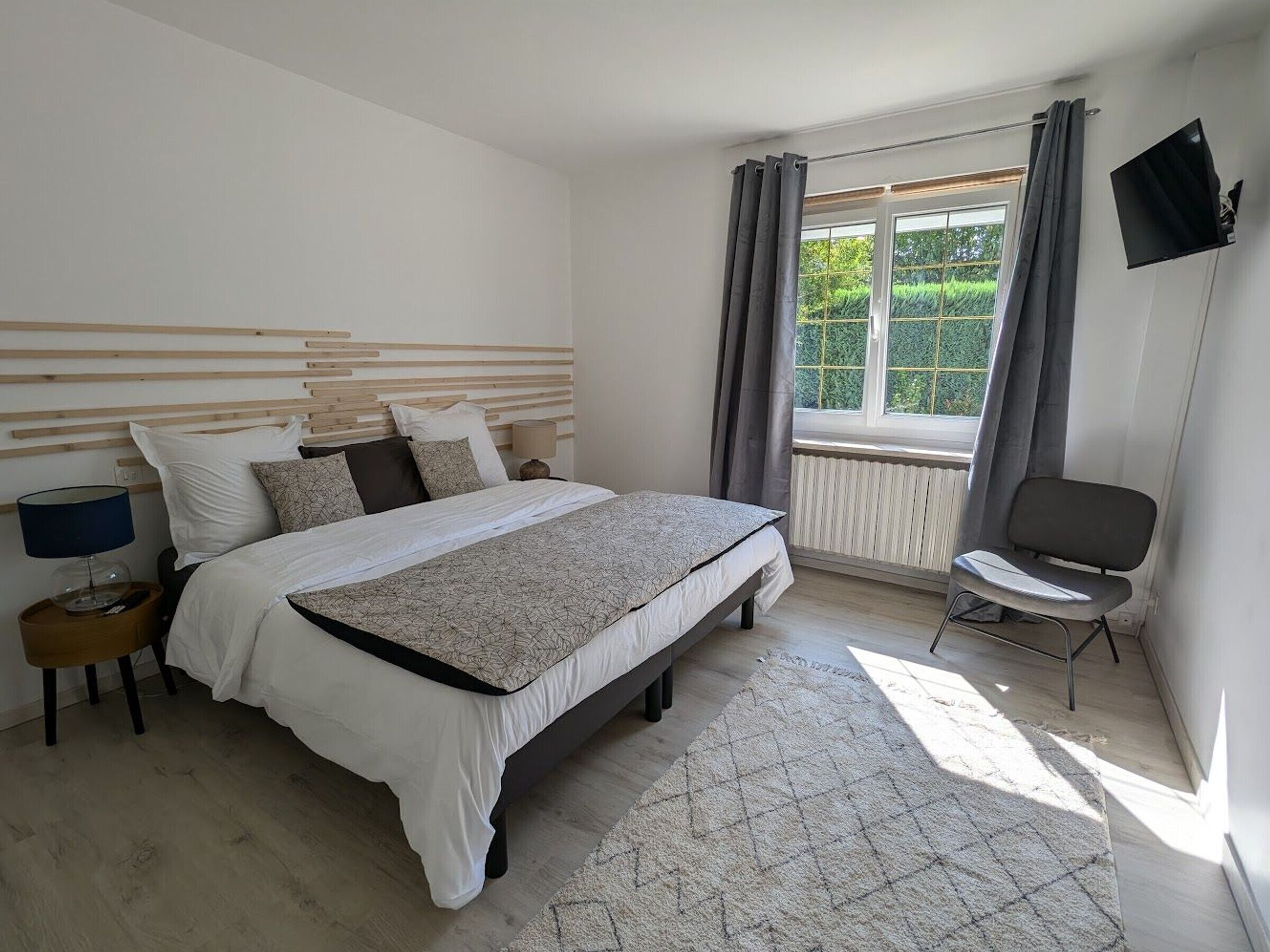 A bedroom with a bed, bedside table, chair, and a window with curtains.