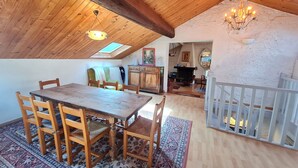 Ein geräumiges Loft mit hoher Decke, Holzbalken, einem Essbereich mit großem Tisch und Stühlen sowie einer gemütlichen Sitzecke mit einer Couch und einem Kamin.