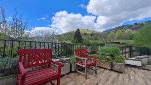 Eine Holzterrasse mit zwei roten Bänken, einem schwarzen Metallgeländer und Blick auf eine Berglandschaft.