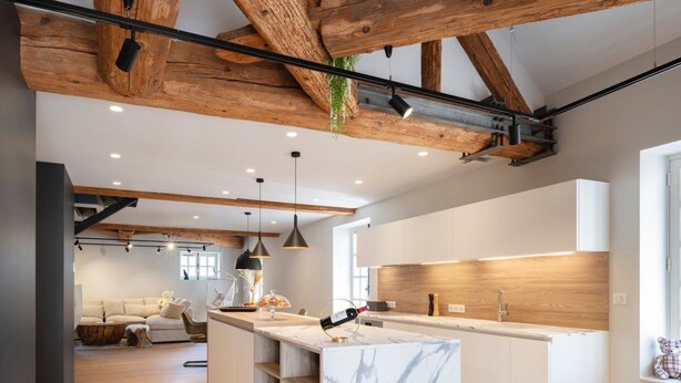 Una cocina moderna con encimeras de mármol, vigas de madera e iluminación colgante.
