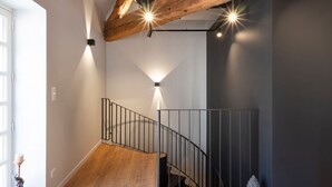 Una escalera con techo de vigas de madera, barandilla metálica y luces fijadas a la pared.