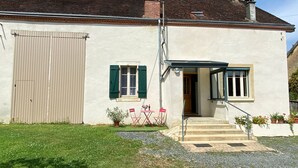 A two-story house with a garage door, a small porch with a table and chairs, and a staircase leading to the entrance. - Charming farmhouse with private garden and pond, perfect for exploring Berry (Gournay)