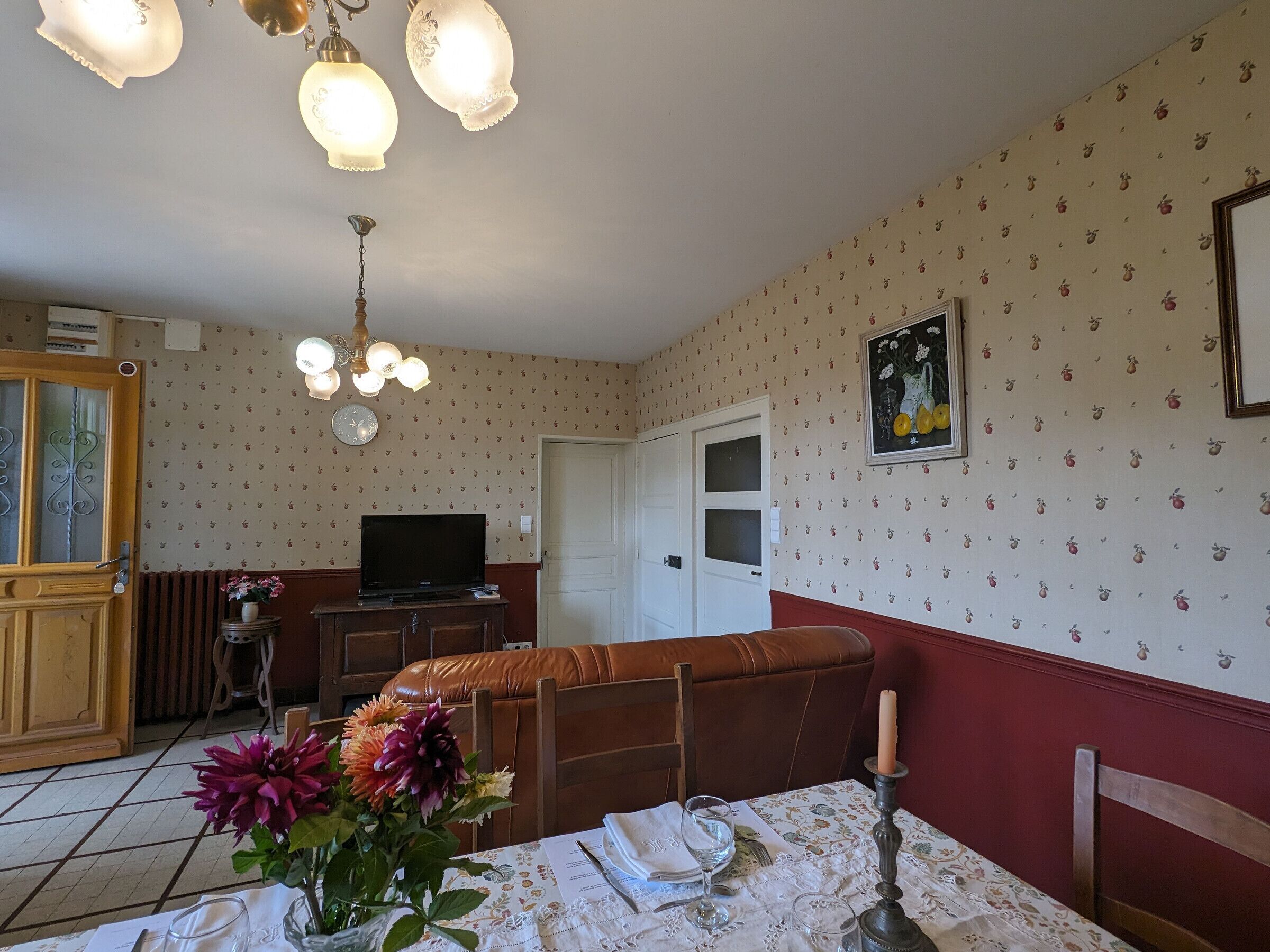 A dining area with a table set for two, a television, and a floral wallpaper pattern.