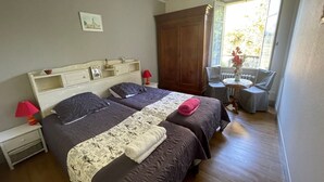 A double room with two beds, a small table, a chair, a window with a view, and a wooden wardrobe. - Charming farmhouse with private garden and pond, perfect for exploring Berry (Gournay)