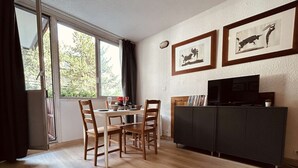 A dining area with a table set for four, a dark-colored entertainment unit, and two framed pictures on the wall.