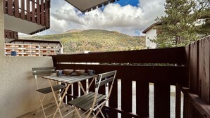 A balcony with a table and chairs, a view of a mountain, and a wooden fence.
