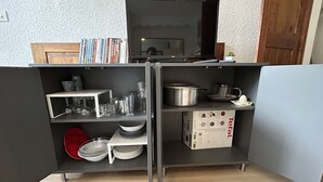 A compact kitchen with a built-in TV, shelves with kitchenware, and a refrigerator.