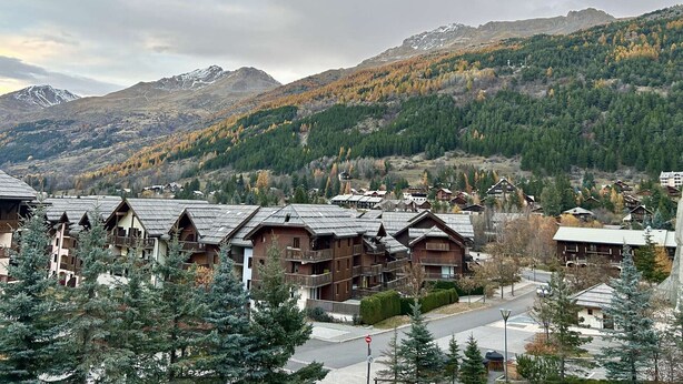 A mountain resort with chalet-style buildings, a road, and a view of snow-capped mountains.