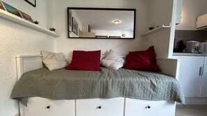 A bedroom with a bed, a dresser, a mirror, and a kitchenette.
