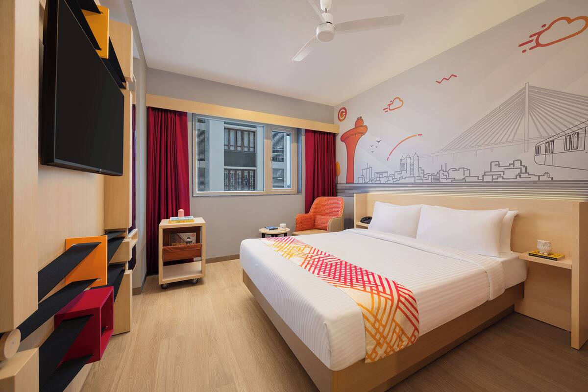 Ein Hotelzimmer mit einem großen Bett, einem Schreibtisch, einem Stuhl, einem Fernseher und einem Fenster mit Vorhängen.