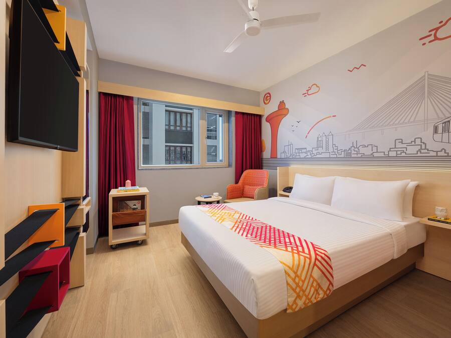 A hotel room with a large bed, a desk, a chair, a TV, and a window with curtains.