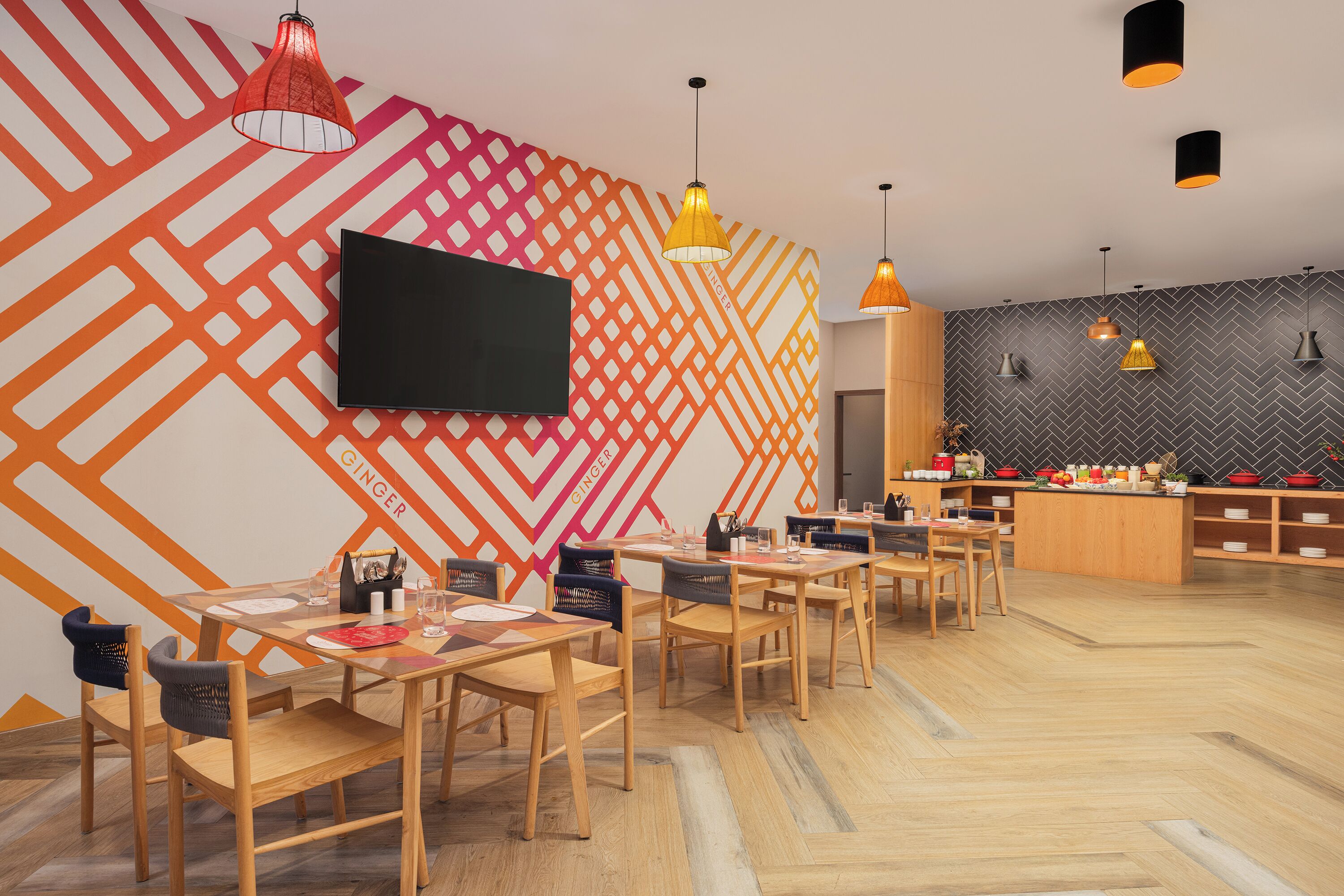 Un restaurant moderne avec des tables et des chaises en bois, un téléviseur à écran plat et un mur orné d’un motif en chevrons.