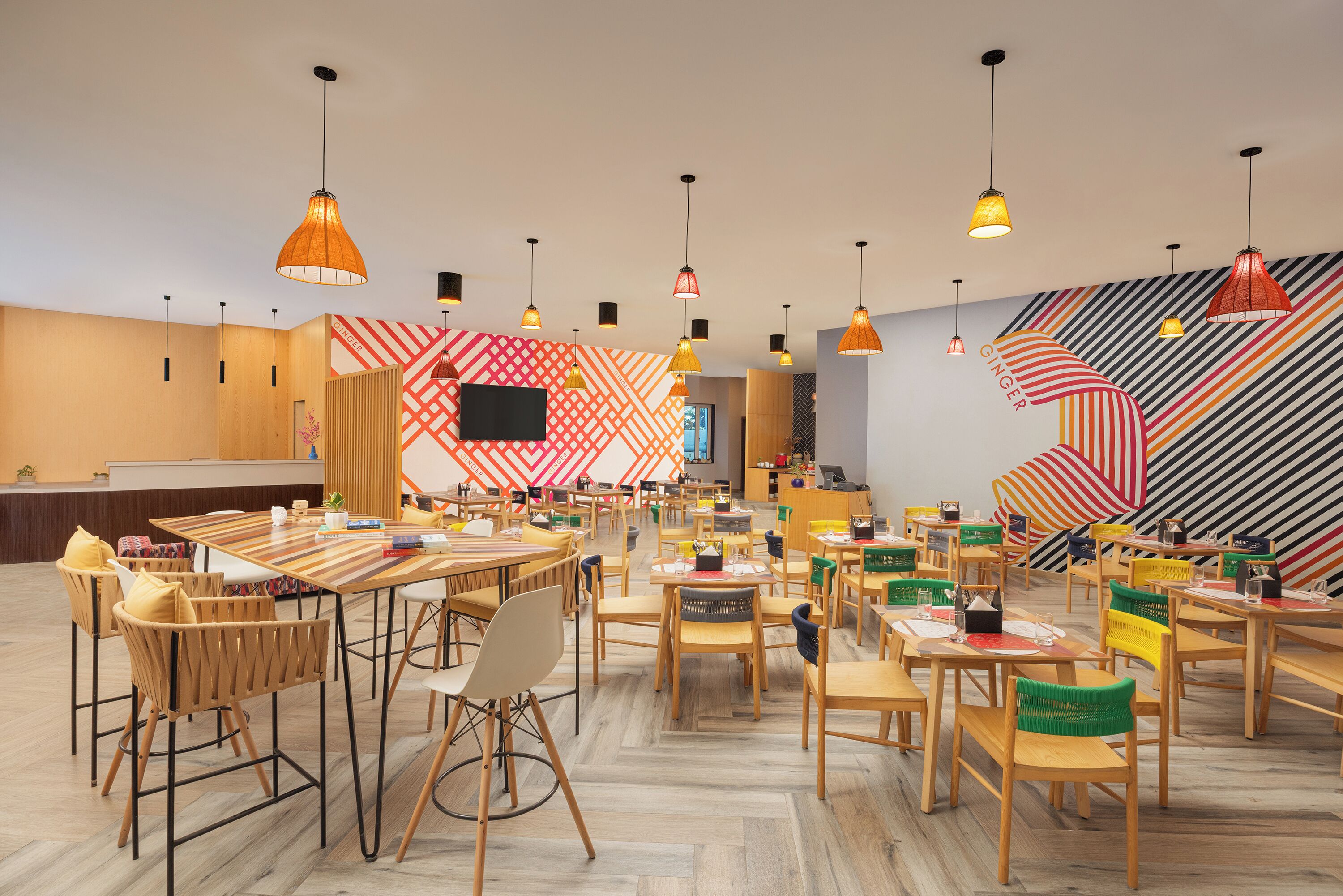 A spacious dining area with multiple tables and chairs, a variety of pendant lights, and a vibrant wall design.