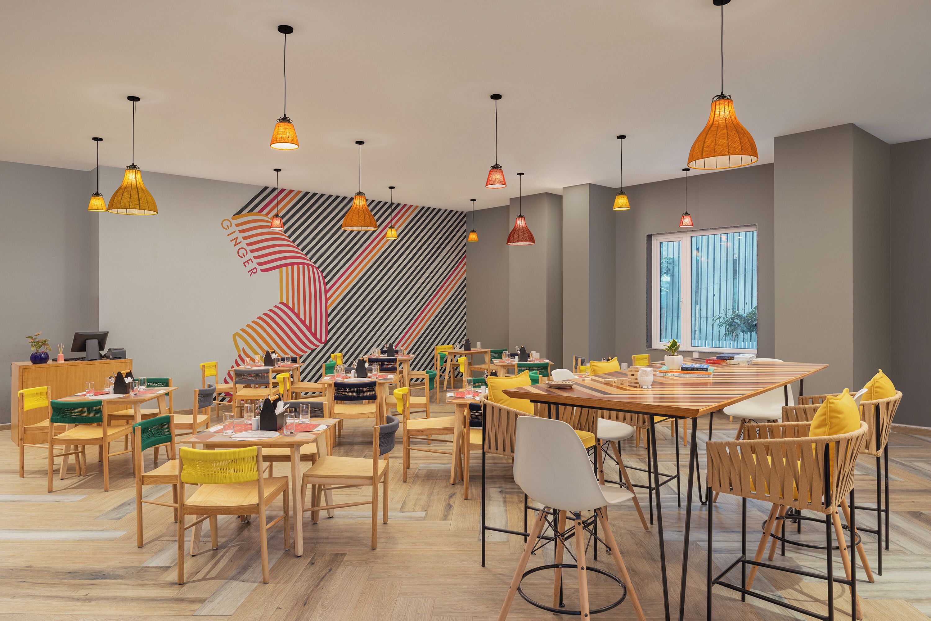 A modern dining area with wooden tables and chairs, striped wall decor, and pendant lighting.