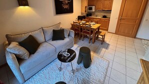 Un salon comprenant un canapé, une table basse et une table à manger avec des chaises. Il y a également un coin cuisine avec des placards et un four à micro-ondes.
