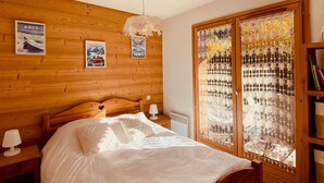 Une chambre confortable avec une tête de lit en bois, un lit recouvert de draps blancs, une table de chevet avec une lampe et une fenêtre ornée de rideaux en dentelle décorative.