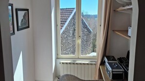 Habitació petita i lluminosa amb una finestra gran, una cadira de vimetla, un radiador i una taula petita amb una placa de cocció.
