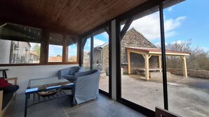 Habitació amb paret de vidre, sostre de fusta, sofà, taula i edifici de pedra a l'exterior.
