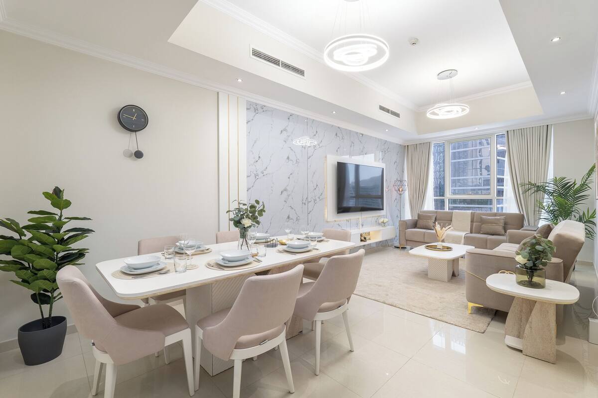 Un salon moderne comprenant un coin repas, un téléviseur à écran plat fixé au mur et une grande fenêtre laissant entrer la lumière naturelle.