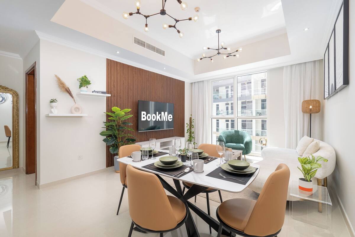 Un espace repas moderne avec une table blanche, des chaises marron et un écran de télévision affichant l'application « BookMe ».