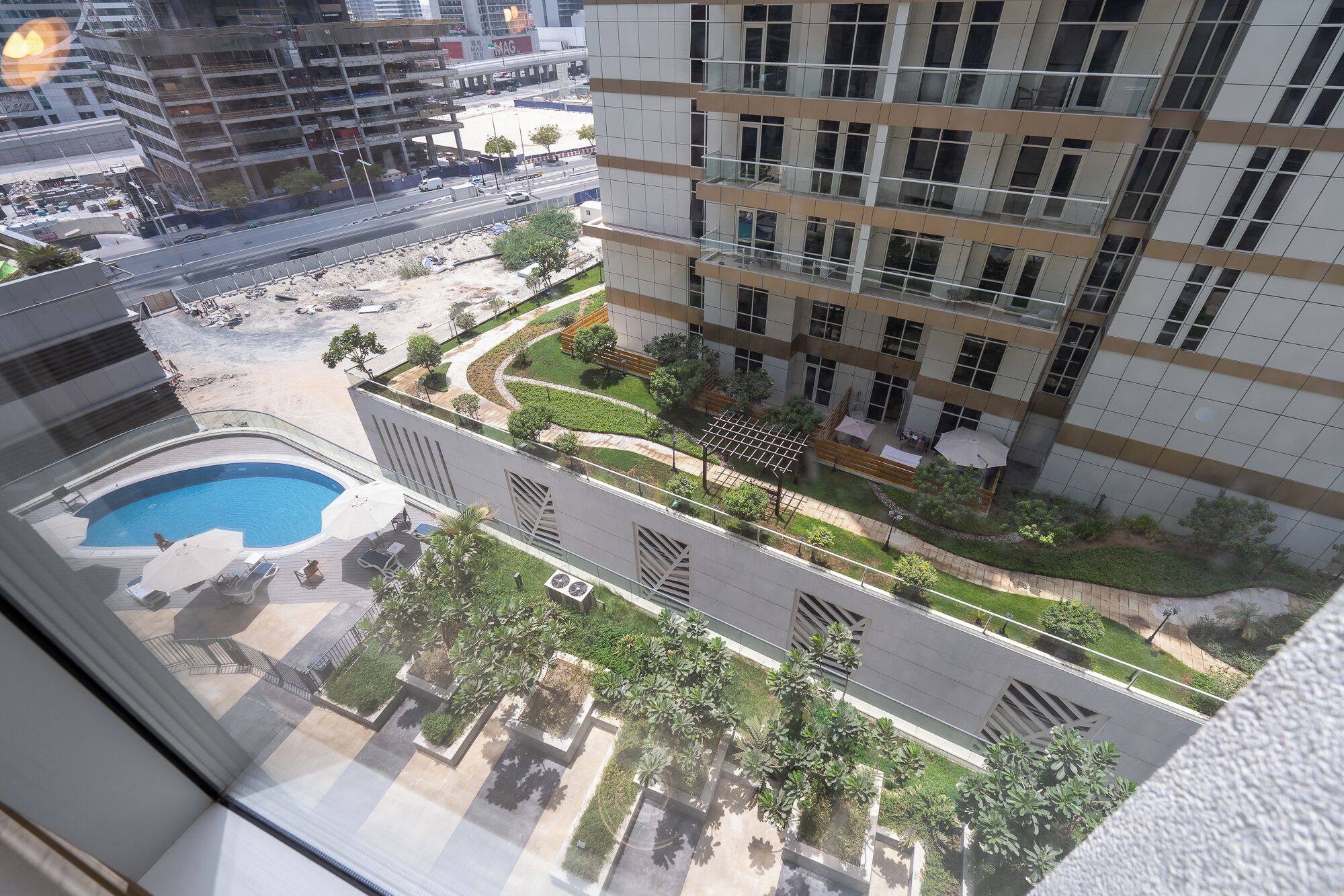 A high-rise building with a rooftop pool, a landscaped garden, and a view of a busy street below.