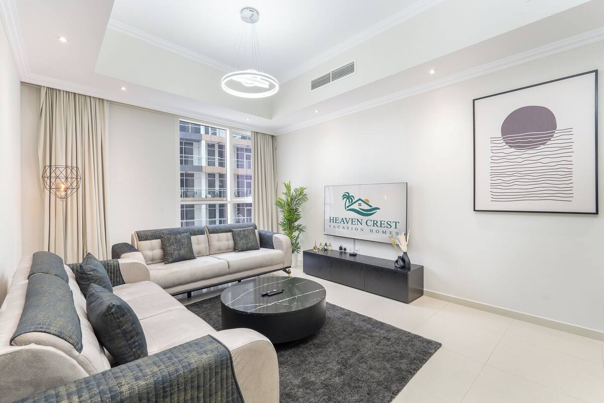 Un salon moderne avec un canapé, une table basse et un téléviseur diffusant une publicité pour « Heaven Crest Vacation Homes ».