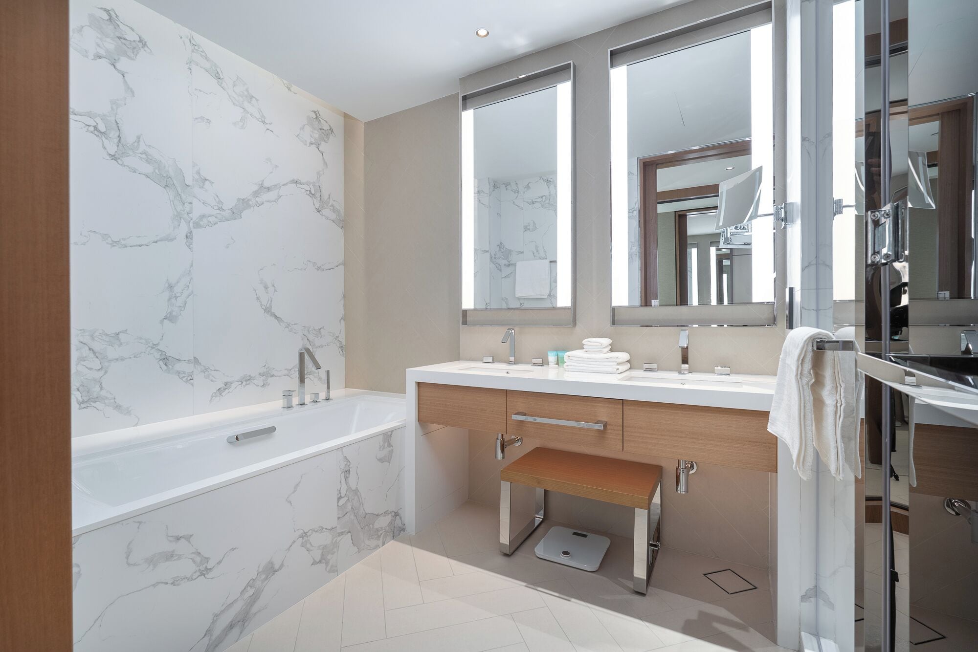 A modern bathroom with a marble wall, a bathtub, a vanity with a mirror, and a shower area.