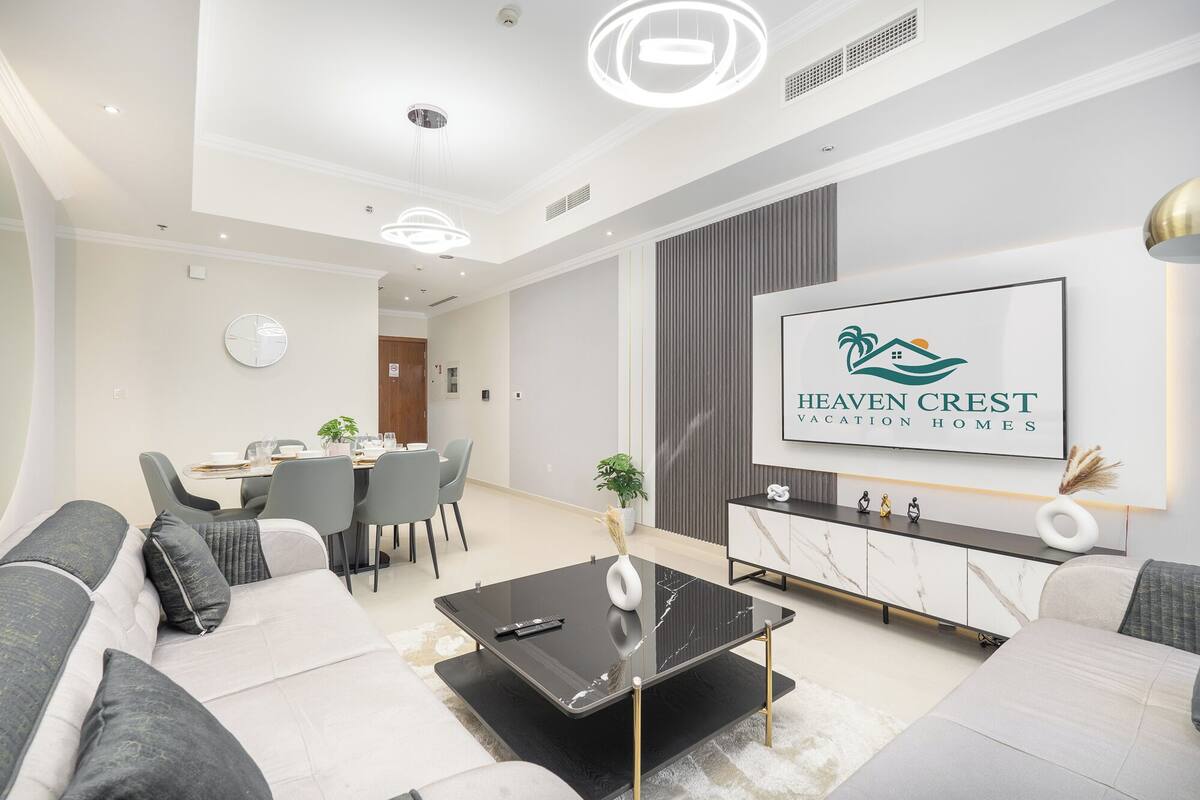 Un salon moderne comprenant un ensemble de canapés, un coin repas avec des chaises et une table, ainsi qu’un grand panneau décoratif encadré accroché au mur.
