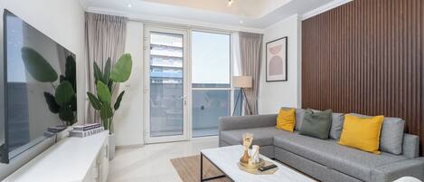 A modern living room with a grey sofa, a coffee table, a TV, and a large window with curtains.