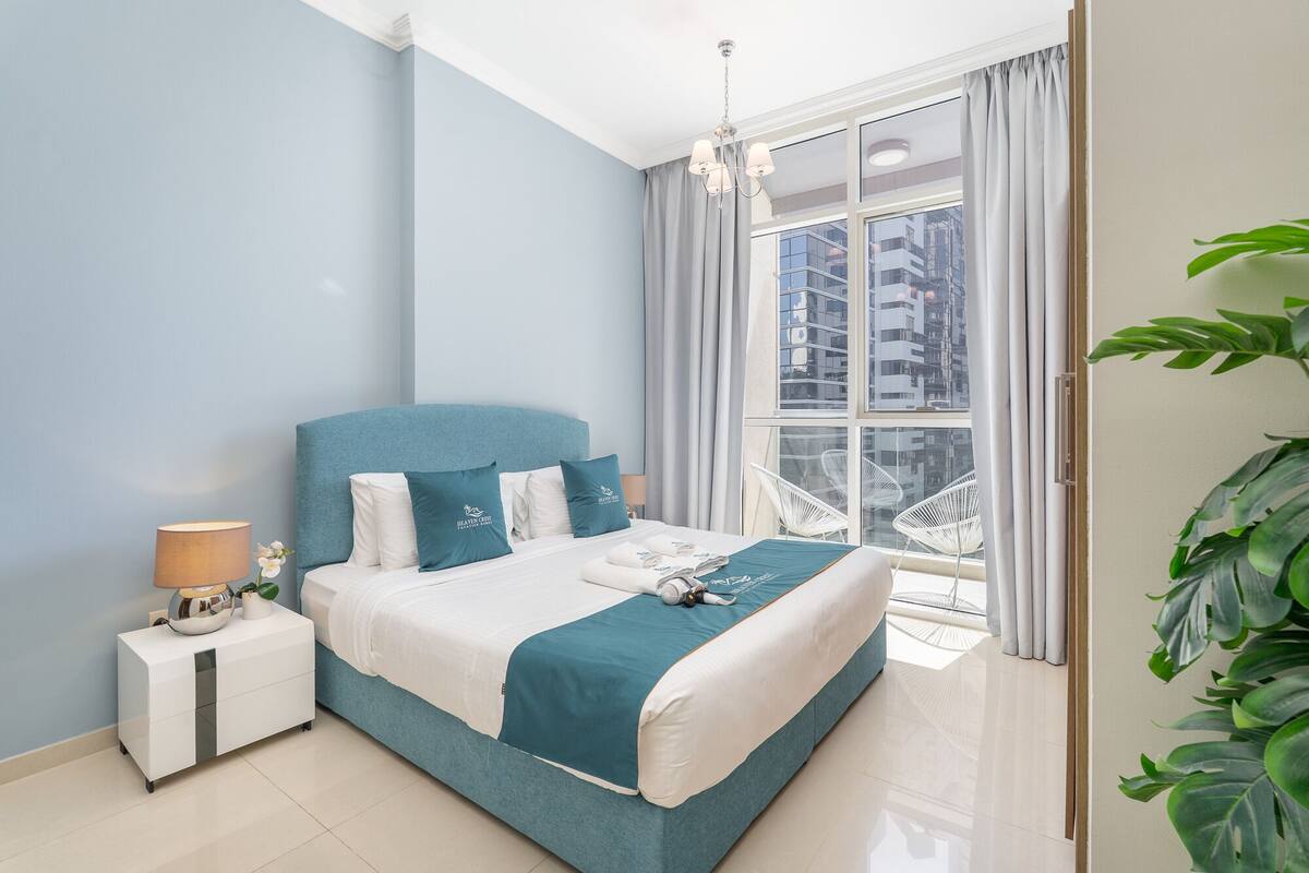 Une chambre moderne avec un lit, une table de chevet et une grande fenêtre avec des rideaux.