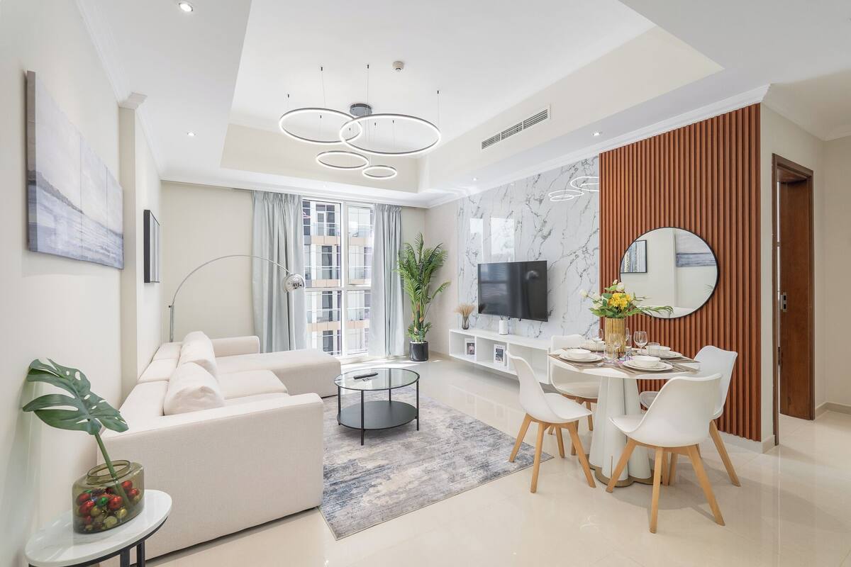 Un salon moderne avec un canapé, une table basse et un coin repas comprenant des chaises et une table dressée pour deux personnes.