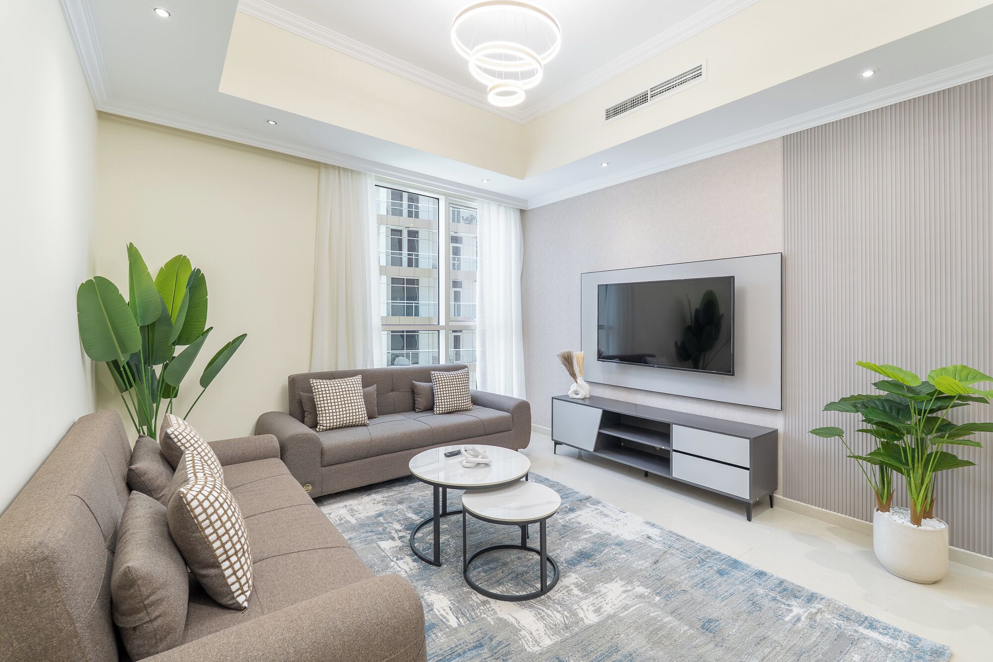 A modern living room with a sofa, coffee table, TV, and potted plants.