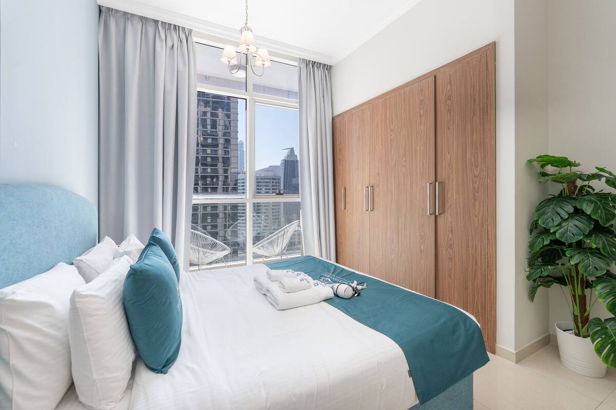Une chambre à coucher avec un lit, une armoire, une fenêtre avec des rideaux et une plante en pot.