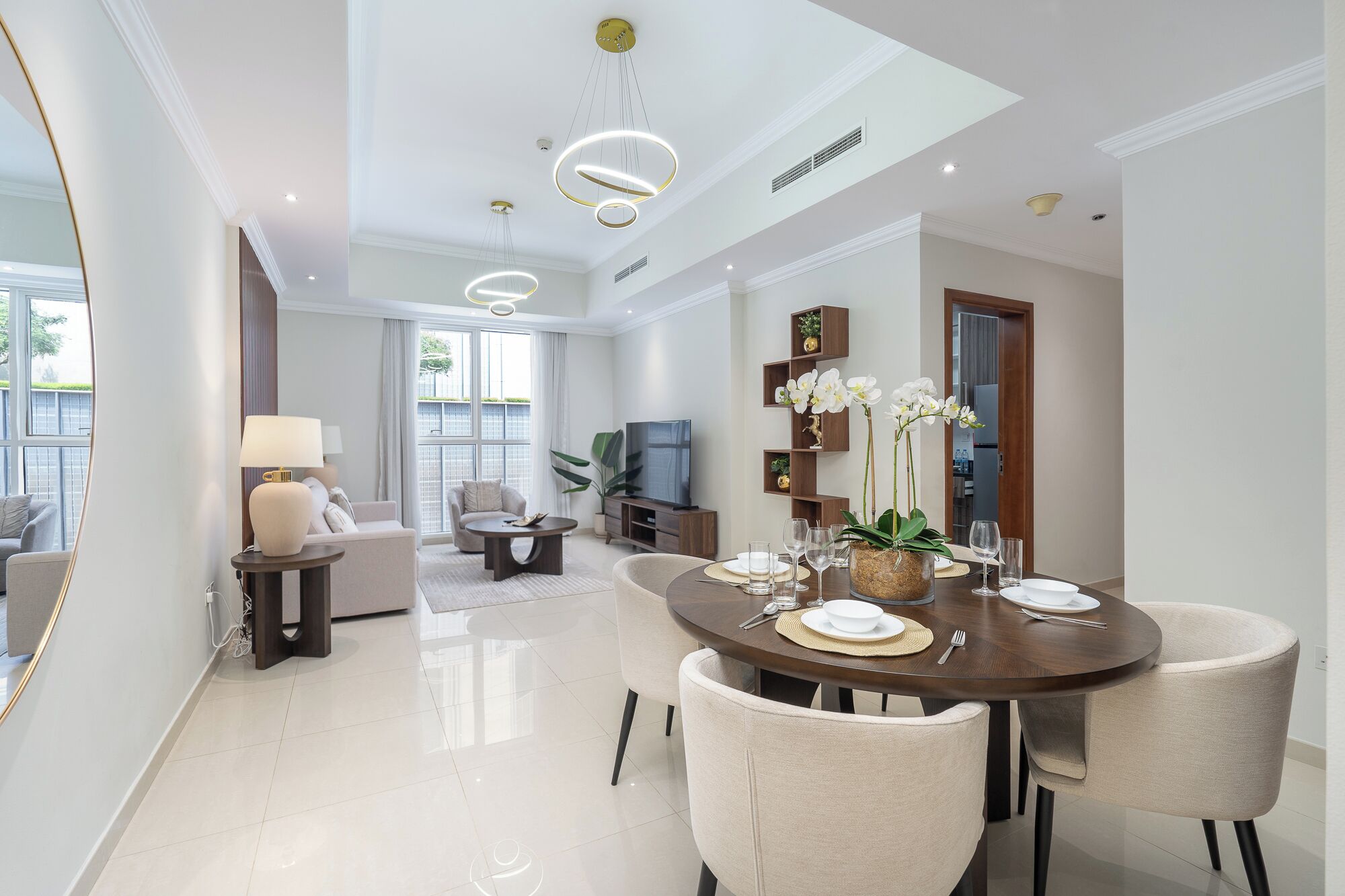 A modern dining area with a round table, chairs, and a TV in the background.